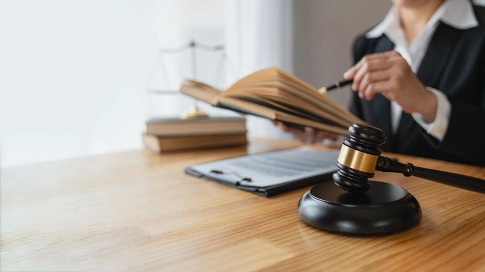 Asian female lawyer or legal advisor working on the scale of justice sitting at her desk and holding a pen to look at the information