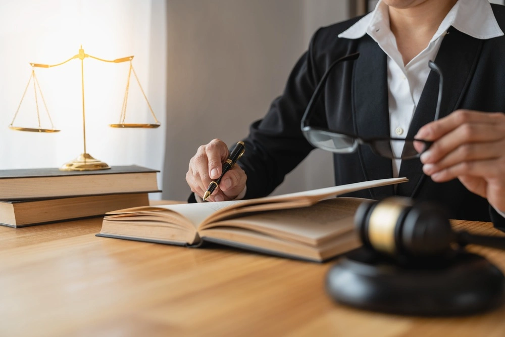 Asian female lawyer or legal consultant working in the justice level sits at her desk holding a pen and removing glasses to relax looking detailed information on the level of jurisprudence to study.